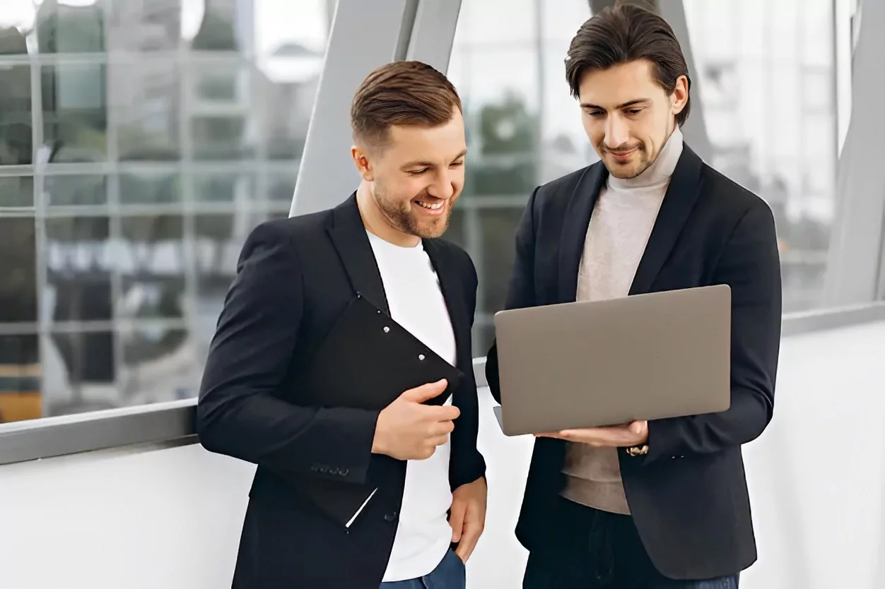 دو مرد در یک محیط حرفه ای در حال بحث و گفتگو و لبخند زدن روی یک لپ تاپ